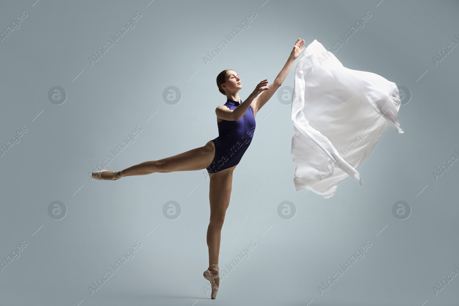 Photo of Graceful young ballerina practicing dance moves with veil on grey background