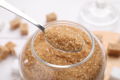 Photo of Taking brown sugar with spoon from jar, closeup