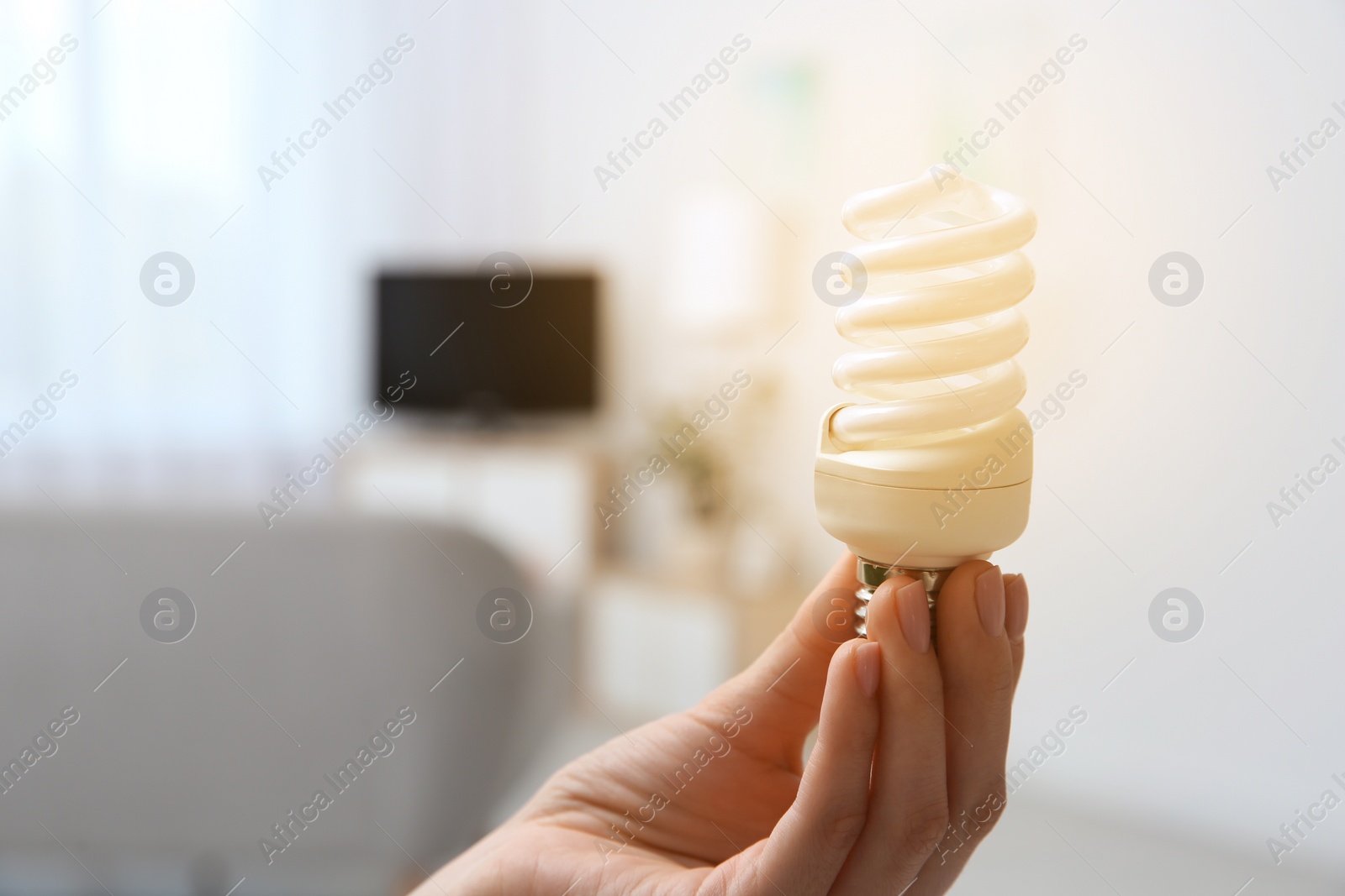 Photo of Woman holding lamp bulb in living room. Space for text