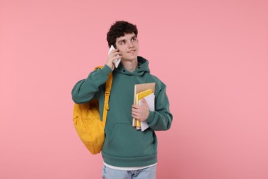Photo of Portrait of student with backpack and notebooks talking on phone against pink background