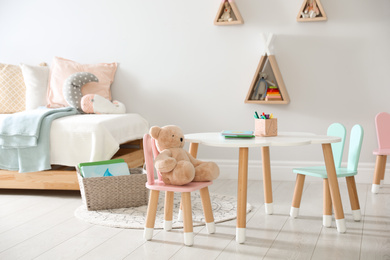 Photo of Small table and chairs with bunny ears in children's room interior