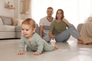 Photo of Happy parents watching their cute baby crawl on floor at home