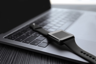 Photo of Stylish smart watch and laptop on table, closeup