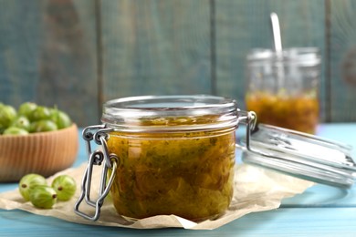 Jar of delicious gooseberry jam and fresh berries on blue wooden table, closeup