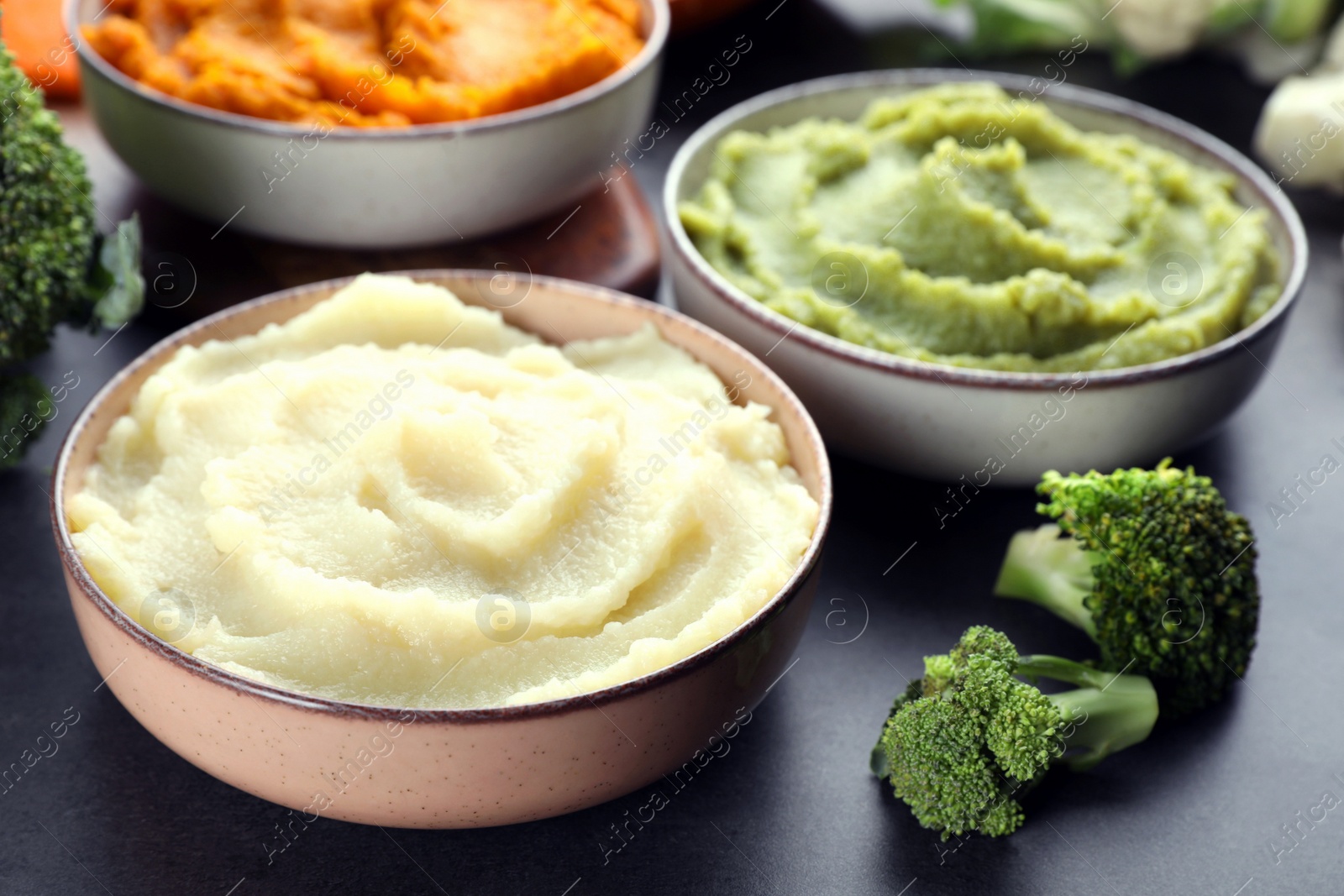 Photo of Bowls with tasty different puree and ingredients on black table, closeup