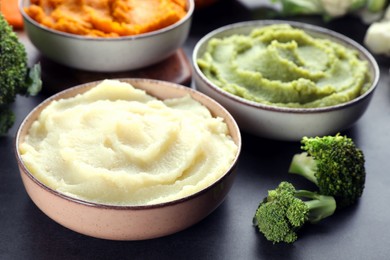 Bowls with tasty different puree and ingredients on black table, closeup