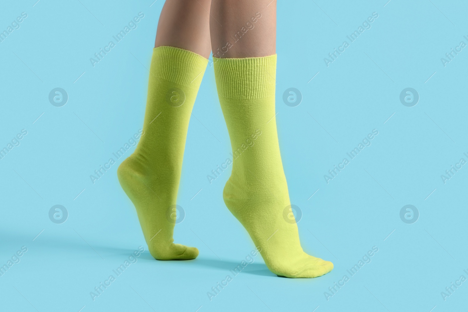 Photo of Woman in stylish yellow socks on light blue background, closeup