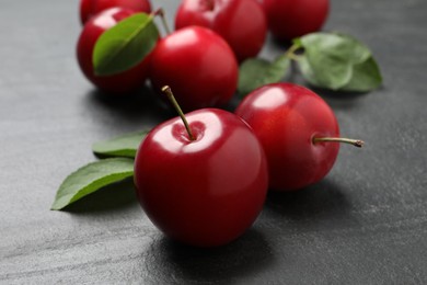Photo of Delicious ripe cherry plums with leaves on black table, closeup