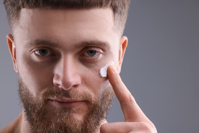 Photo of Handsome man applying moisturizing cream onto his face on grey background, space for text