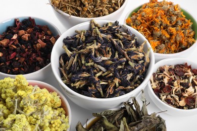 Photo of Many different dry herbs and flowers in bowls on white background, closeup