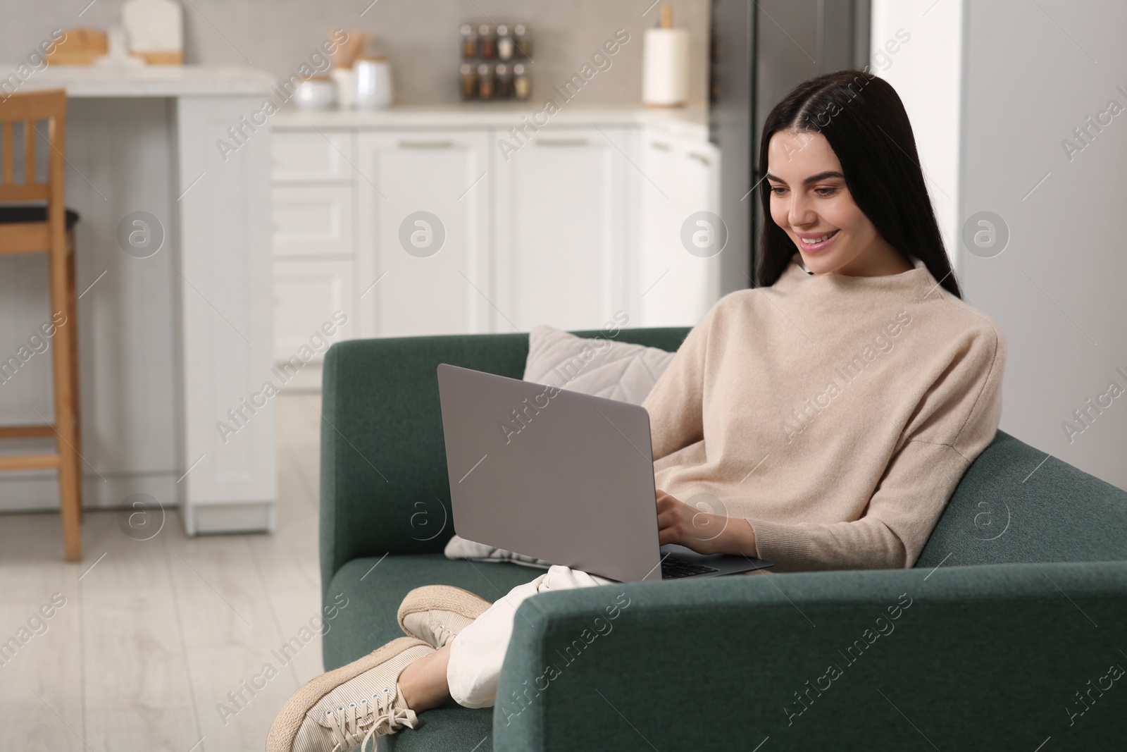 Photo of Happy woman working with laptop on sofa in kitchen