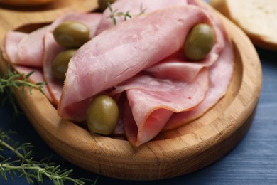 Photo of Slices of delicious ham with olives and thyme on blue wooden table, closeup