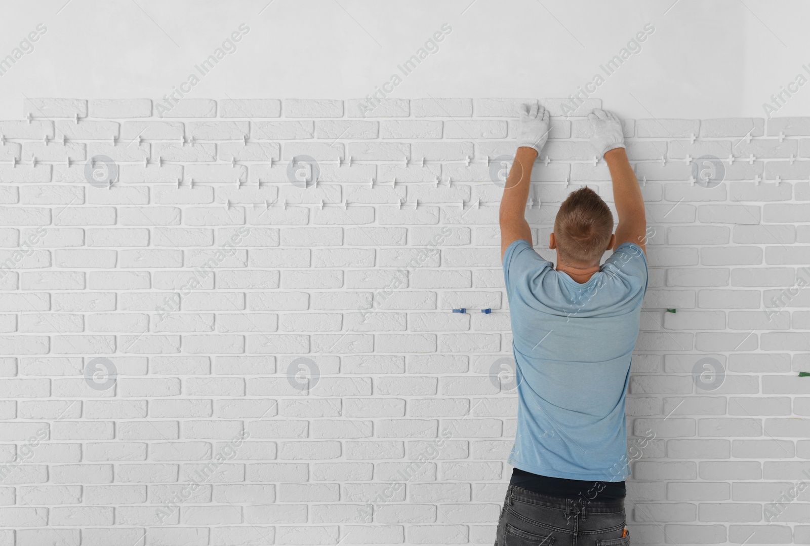 Photo of Professional builder installing new white decorative bricks on wall, back view