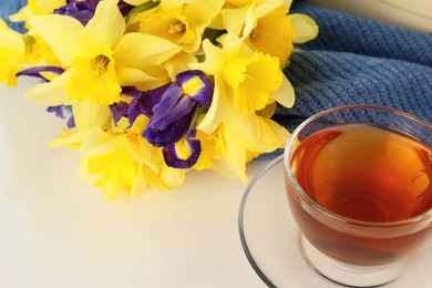 Photo of Cup of aromatic tea, beautiful yellow daffodil and iris flowers on white table, closeup