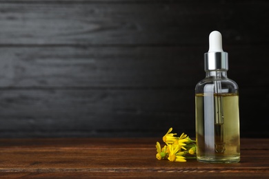 Bottle of essential oil and flowers on wooden table, space for text