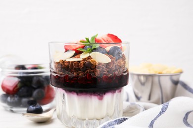 Photo of Tasty granola with berries, jam, yogurt and almond flakes in glass on white table