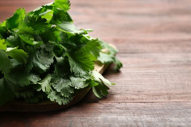Photo of Fresh green coriander leaves on wooden table, closeup. Space for text