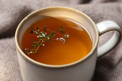 Photo of Cup of aromatic herbal tea with thyme on beige fabric, closeup