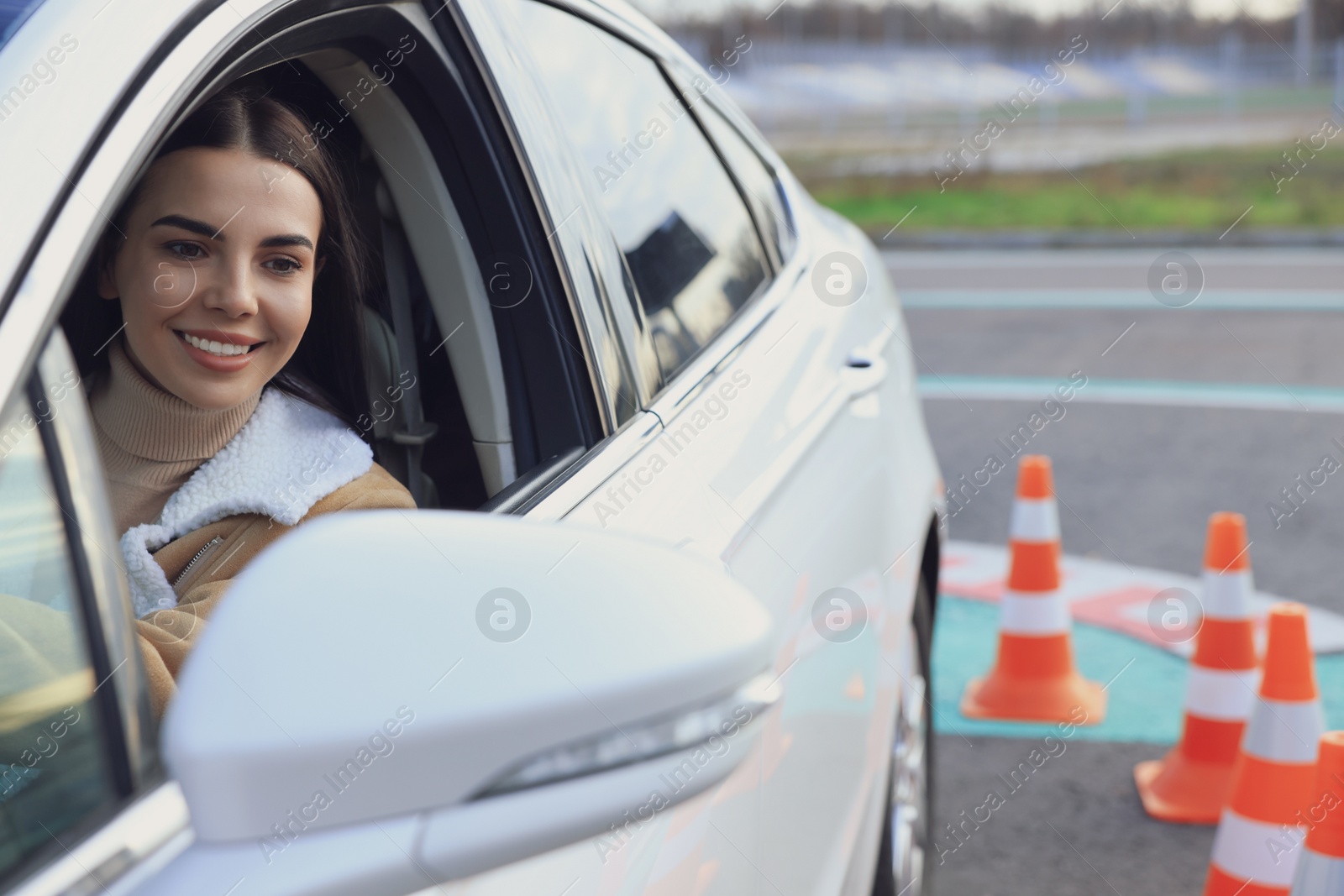 Photo of Young woman in car on test track with traffic cones. Driving school