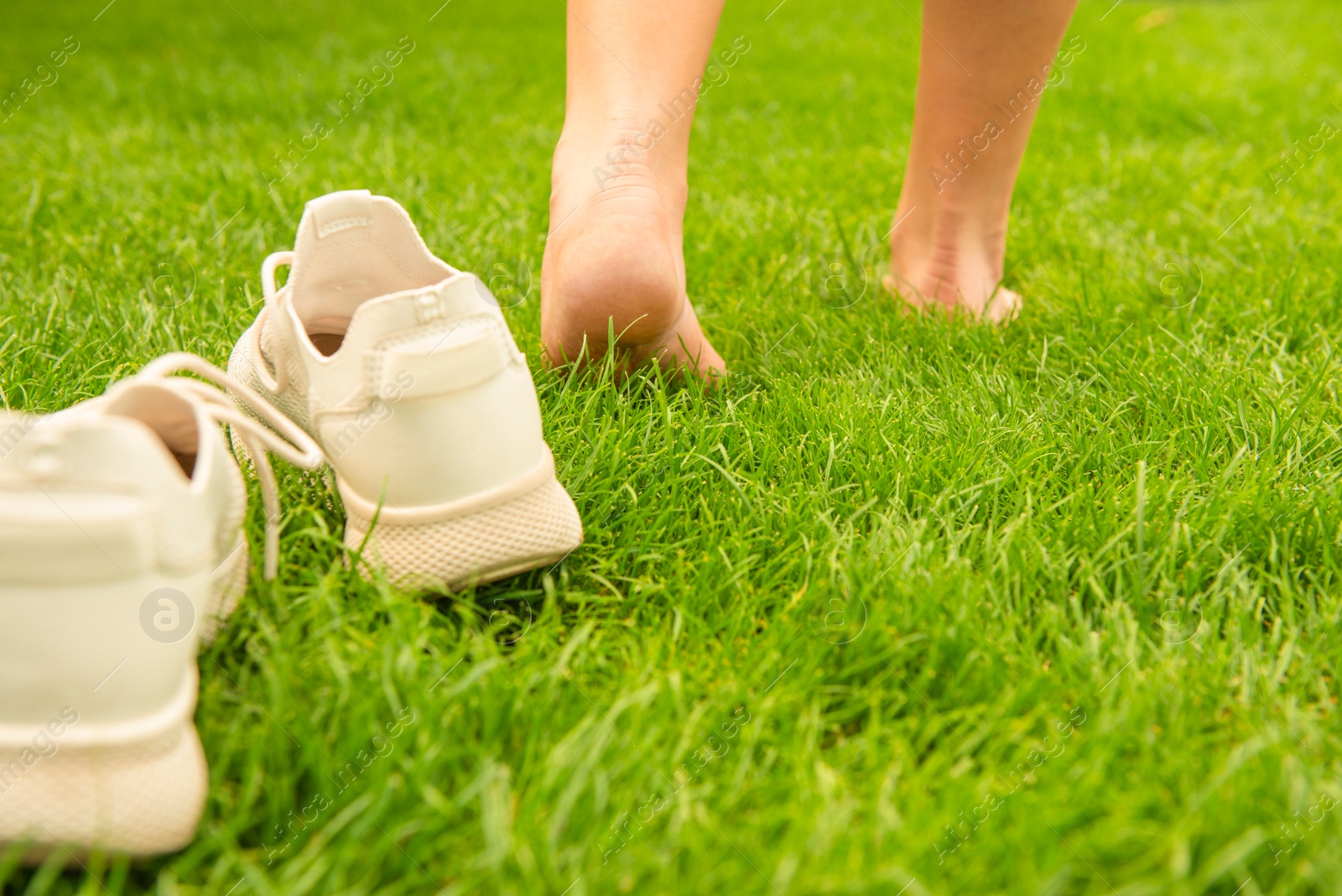 Photo of Woman leaving her sneakers and walking away barefoot on green grass, closeup