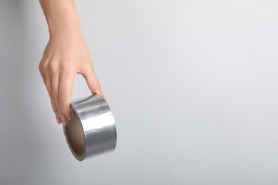 Photo of Woman holding silver adhesive tape on light background, closeup. Space for text