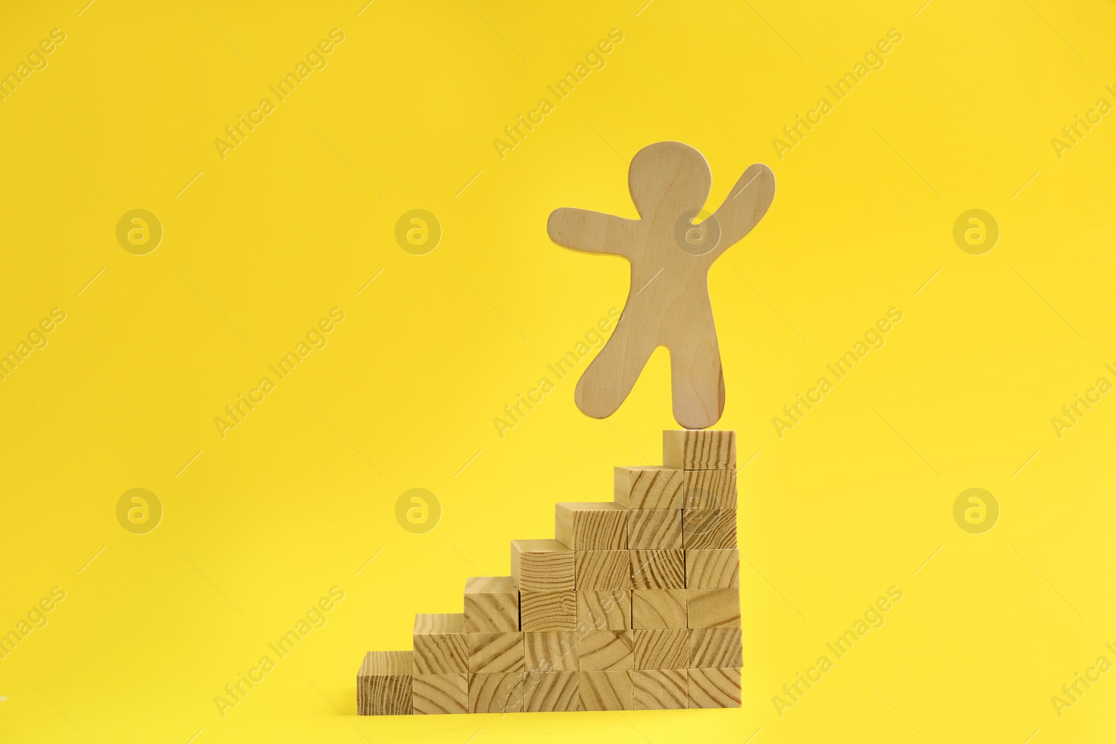 Photo of Wooden human figure on top of stairs against yellow background. Career promotion concept