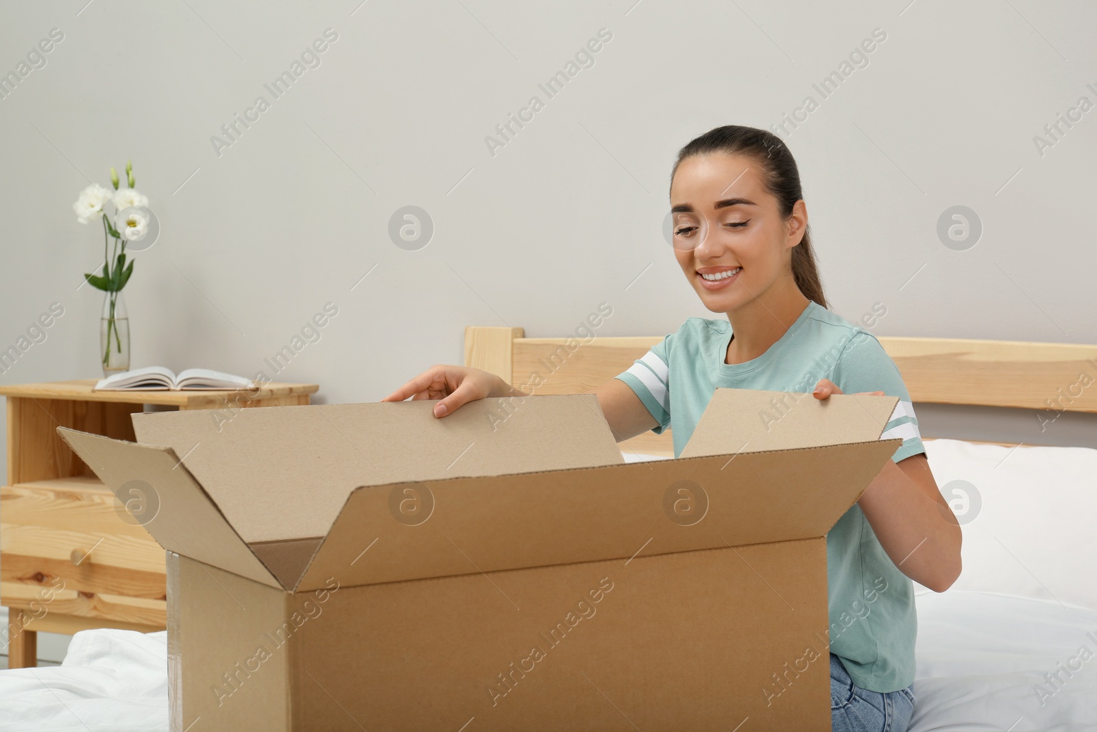 Photo of Happy young woman opening parcel on bed at home. Internet shopping