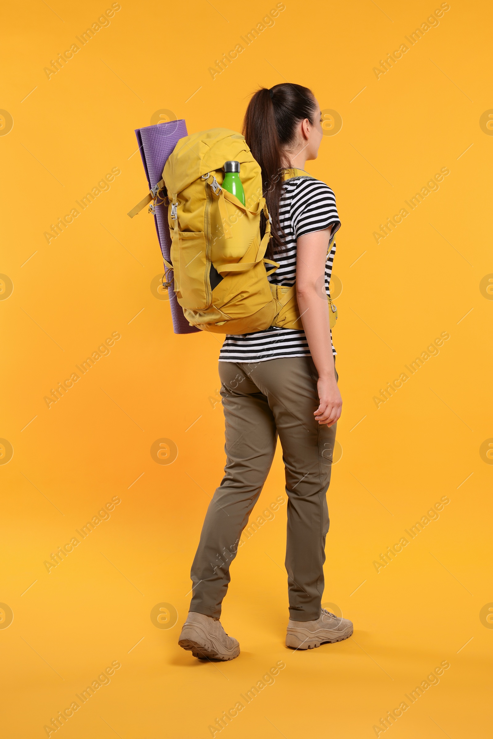 Photo of Woman with backpack walking on orange background. Active tourism