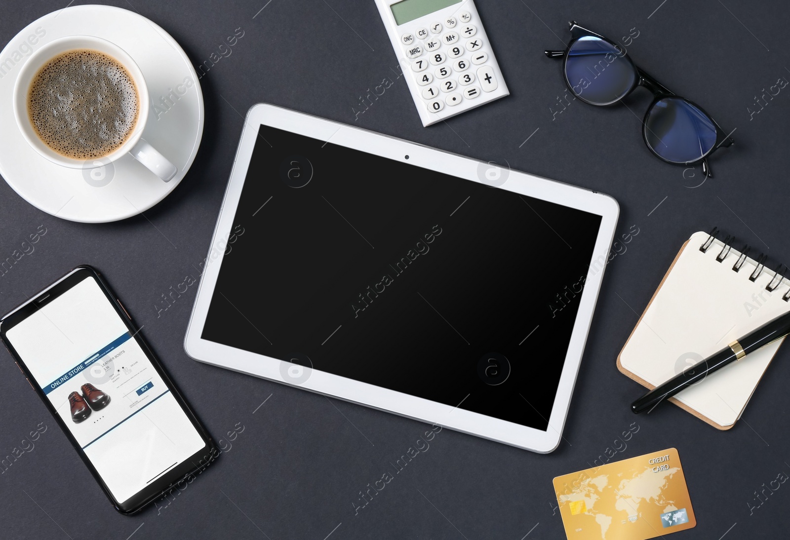 Photo of Online store website on device screen. Tablet, smartphone, credit card, stationery, glasses and coffee on black background, flat lay
