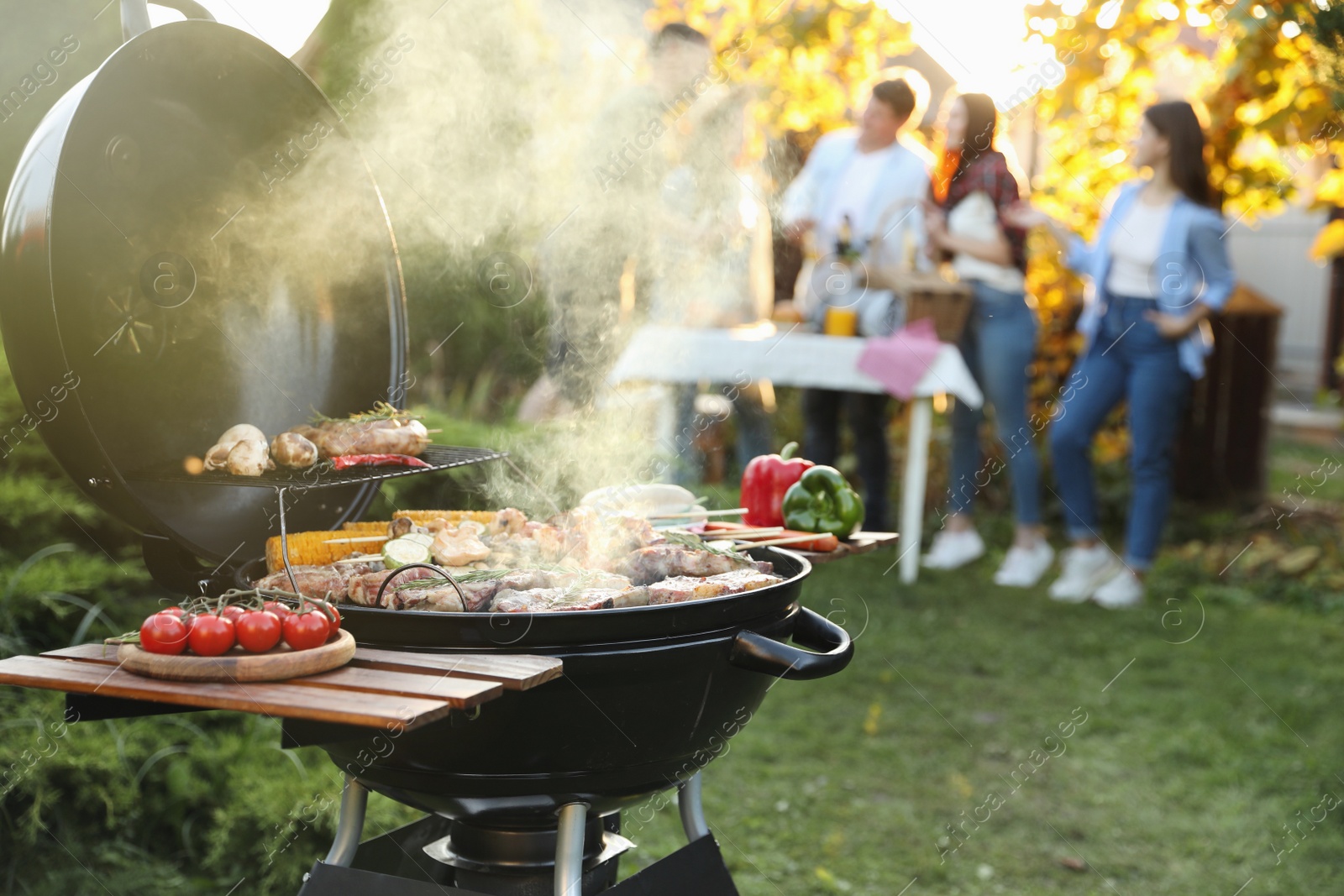 Photo of Group of friends having party outdoors. Focus on barbecue grill with food. Space for text