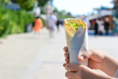 Photo of Woman holding delicious vegetable roll outdoors, closeup. Space for text