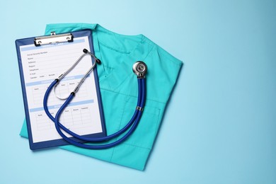 Photo of Medical uniform, stethoscope and clipboard on light blue background, flat lay. Space for text