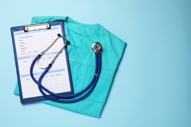 Medical uniform, stethoscope and clipboard on light blue background, flat lay. Space for text