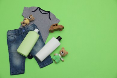 Bottles of laundry detergents, baby clothes and toys on light green background, flat lay. Space for text