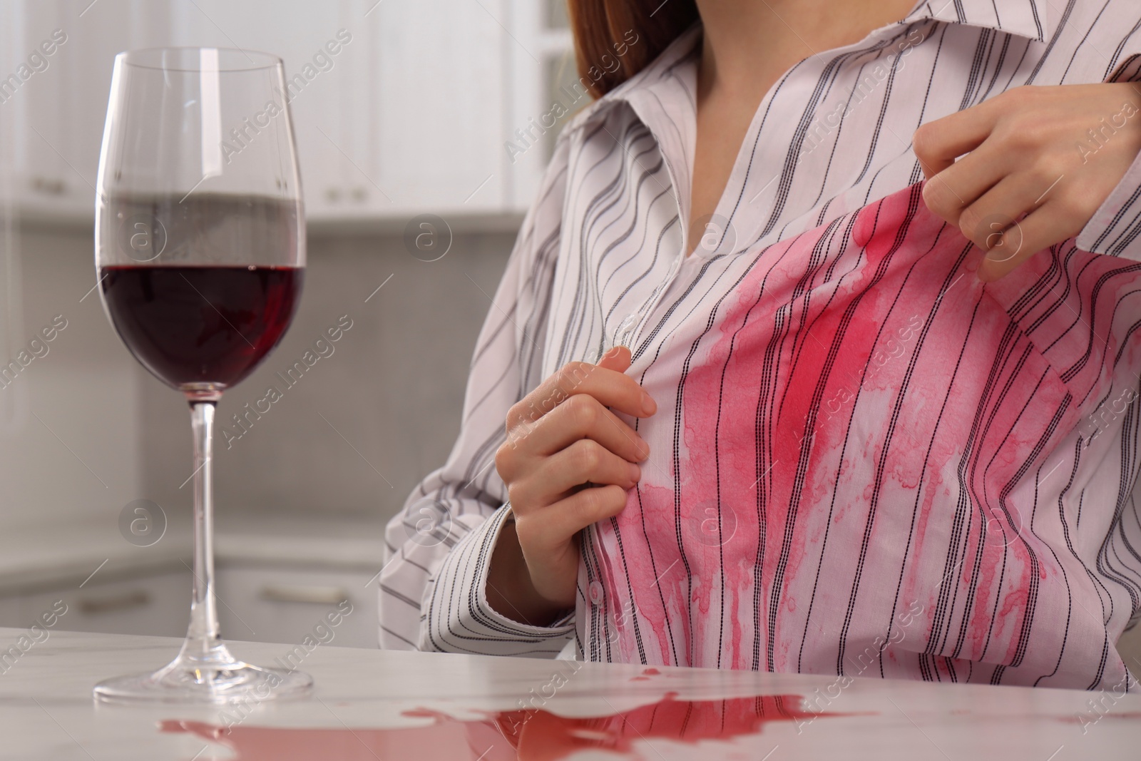 Photo of Woman with spilled wine over her shirt and marble table in kitchen, closeup