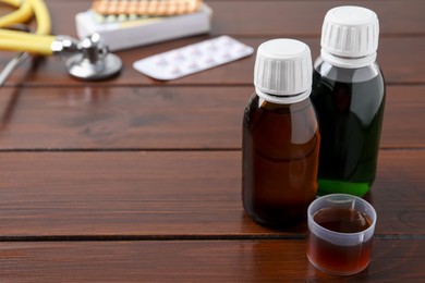 Bottles of syrup and measuring cup on wooden table, space for text. Cold medicine