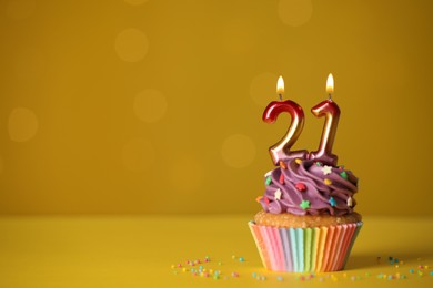 Photo of Coming of age party - 21th birthday. Delicious cupcake with number shaped candles on yellow background, space for text