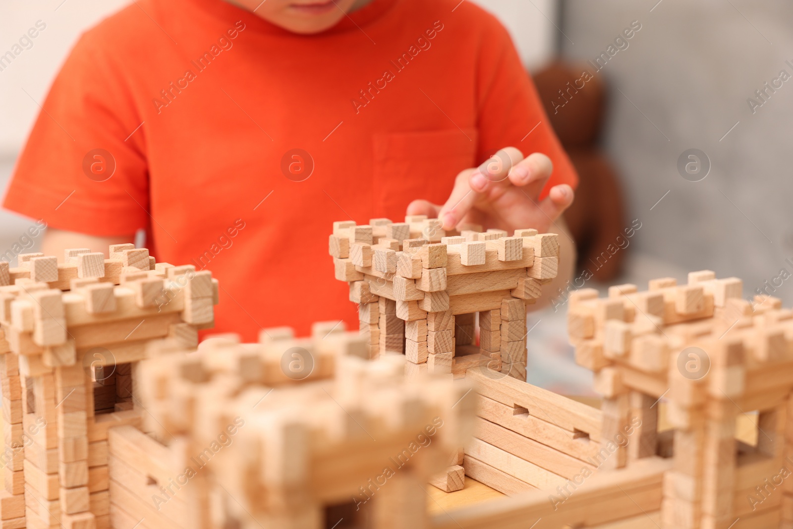 Photo of Little boy playing with wooden construction set at table in room, closeup. Child's toy