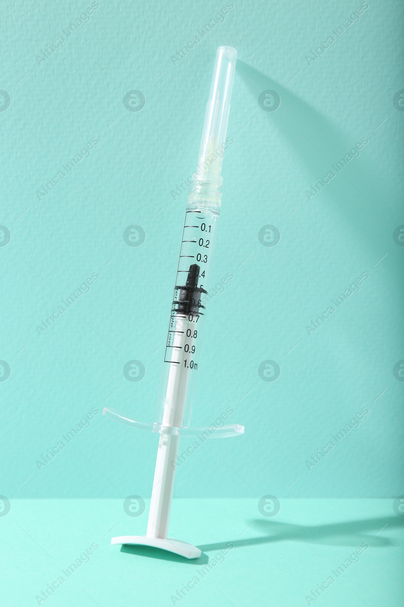 Photo of Cosmetology. One medical syringe on turquoise background