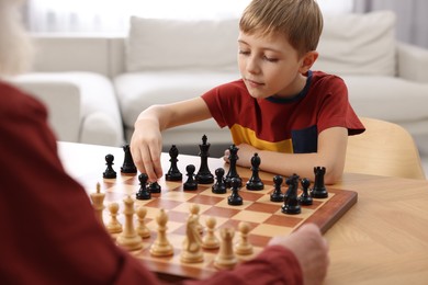 Little boy playing chess with his grandfather at table in room