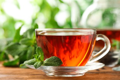 Glass cup of aromatic black tea with fresh mint on wooden table against blurred background, closeup