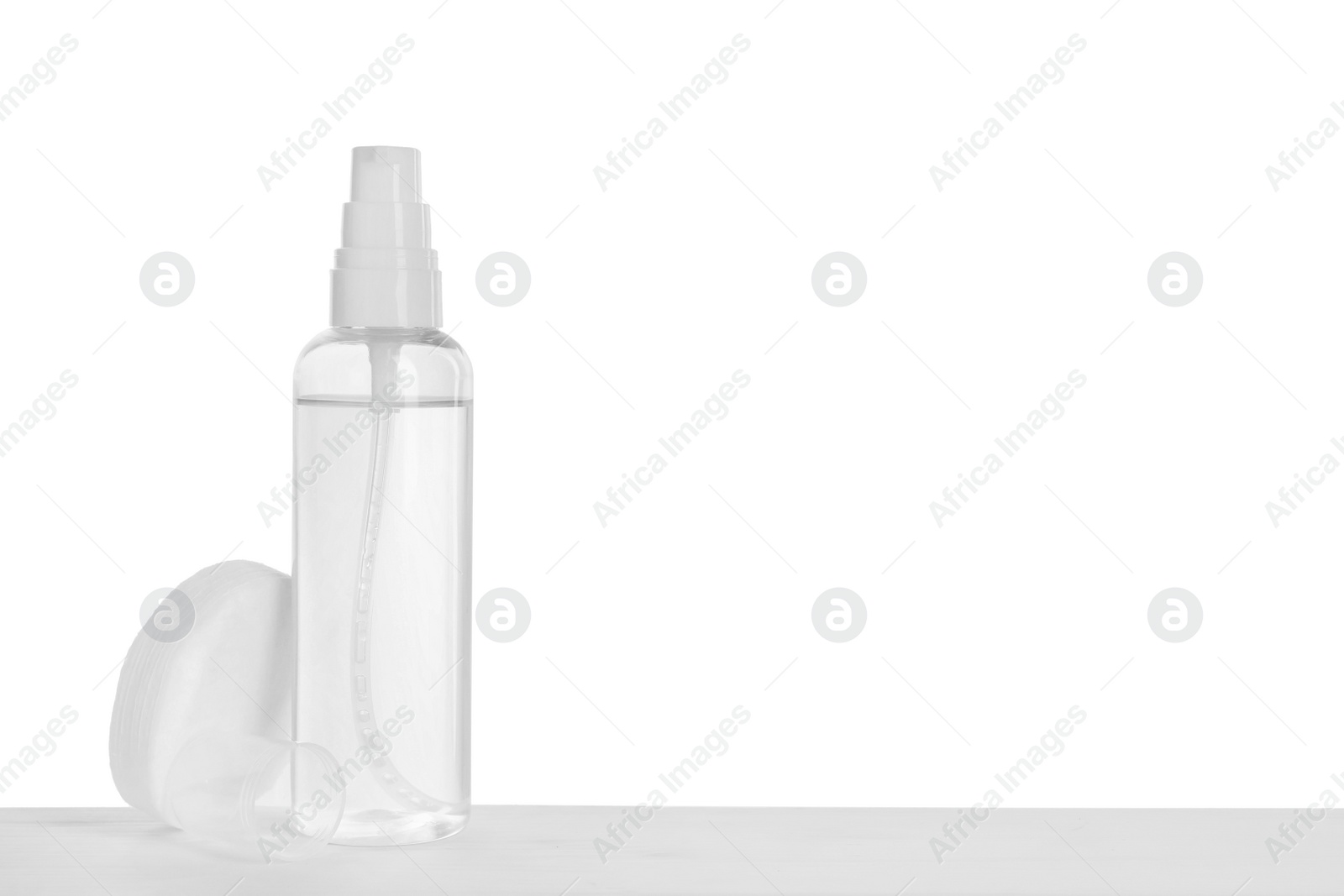 Photo of Micellar water and cotton pads on table against white background. Space for text