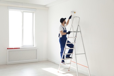 Photo of Handyman painting wall with roller brush indoors, space for text. Professional construction tools