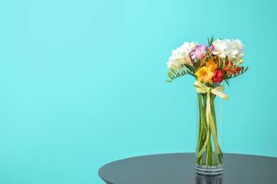 Glass vase with beautiful freesia on table against color background