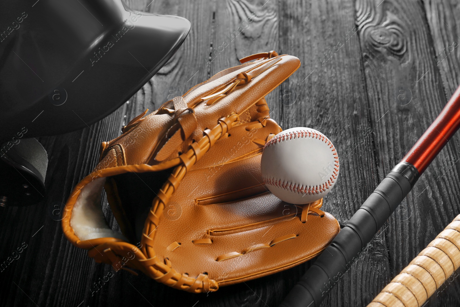 Photo of Baseball glove, bats, ball and batting helmet on black wooden table, closeup