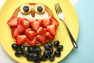 Creative serving for kids. Plate with cute owl made of pancakes, berries, cream, banana and almond on color background, top view