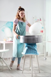 Photo of Young woman making cotton candy using modern machine in room