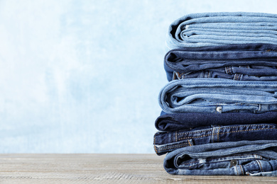 Stack of different jeans on wooden table against blue background. Space for text