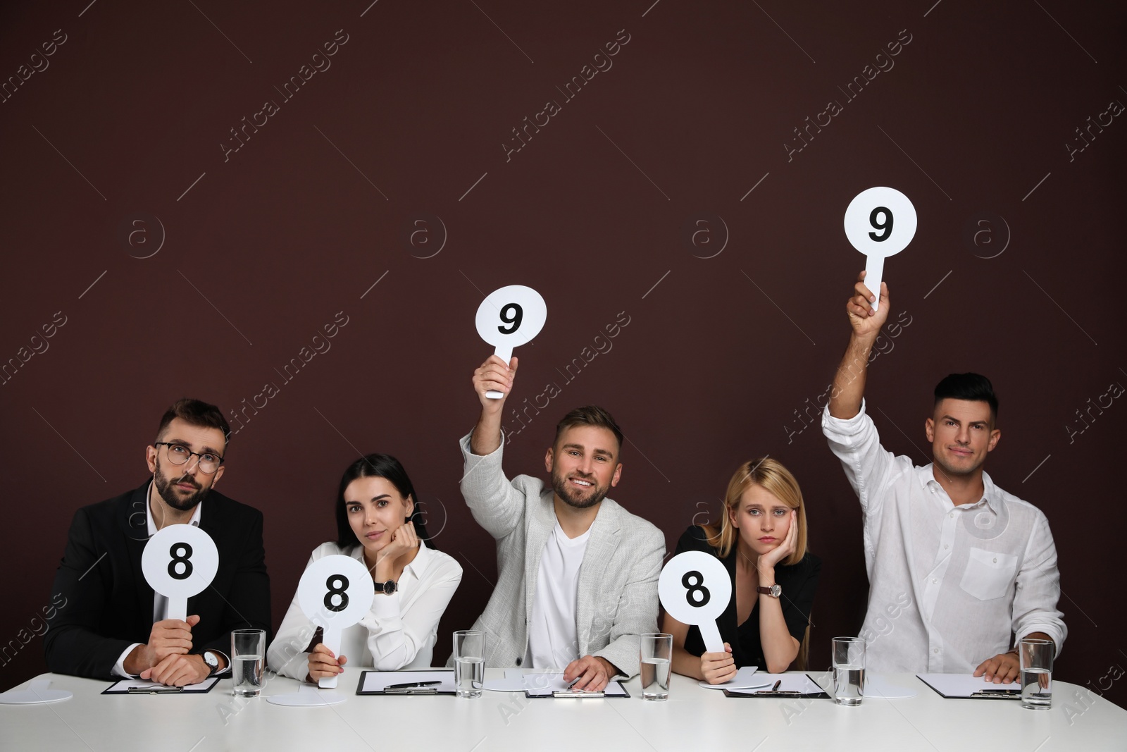 Photo of Panel of judges holding different score signs at table on brown background