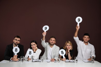 Panel of judges holding different score signs at table on brown background